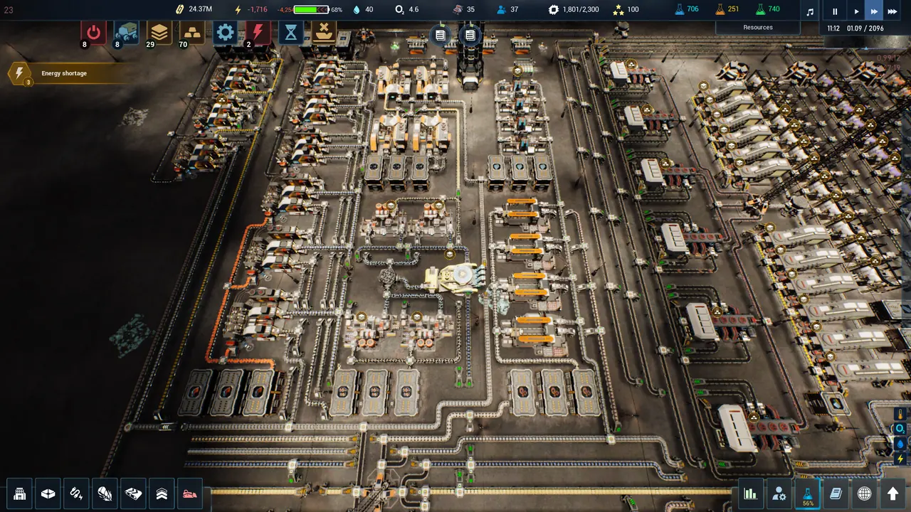 A dense production district seen from above, with conveyor lines threading between blocks of machinery, the HUD resource bar running along the top and an Energy shortage warning panel on the left